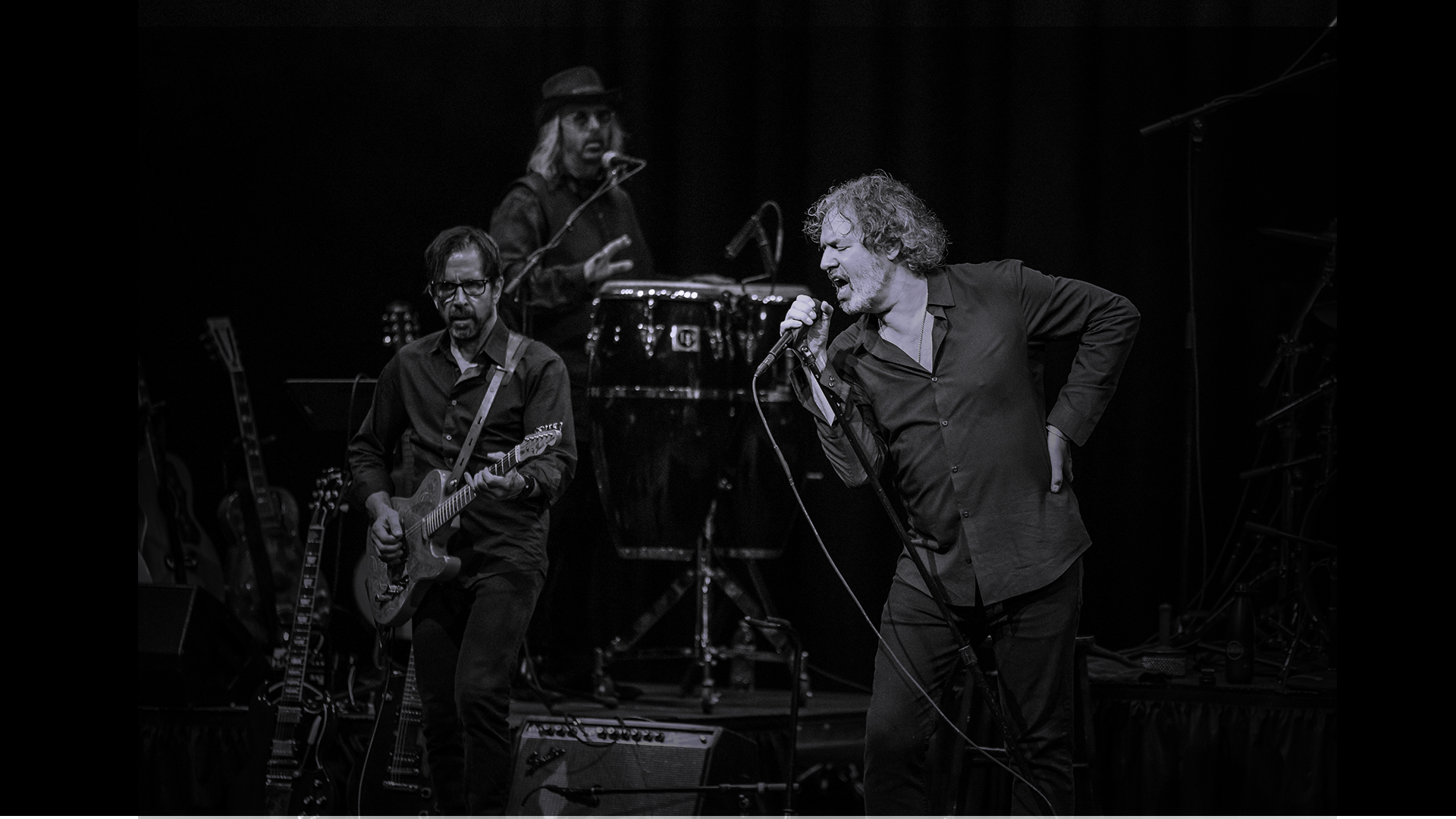 A man singing with a band in the background in black and white