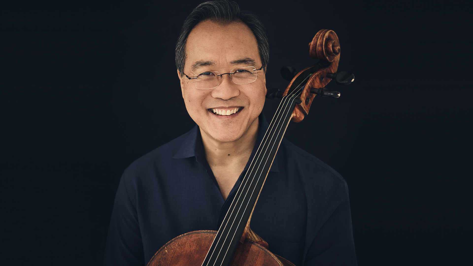A man smiling holding a cello