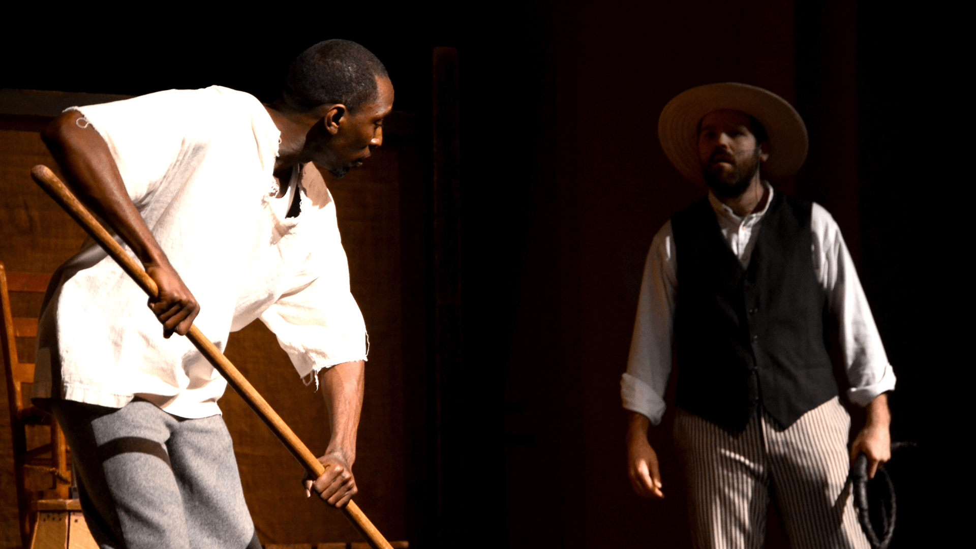 An actor with a farm tool faces another actor in confrontation 