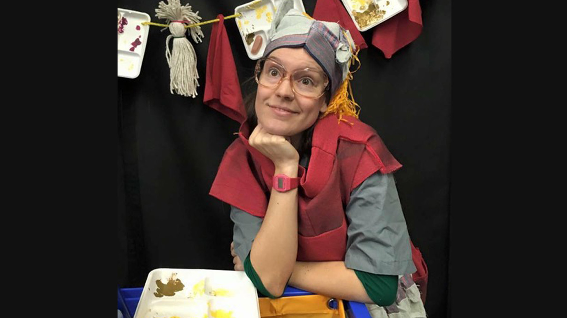 A person wearing glasses sitting at a table with lunch trays hanging up next to them 