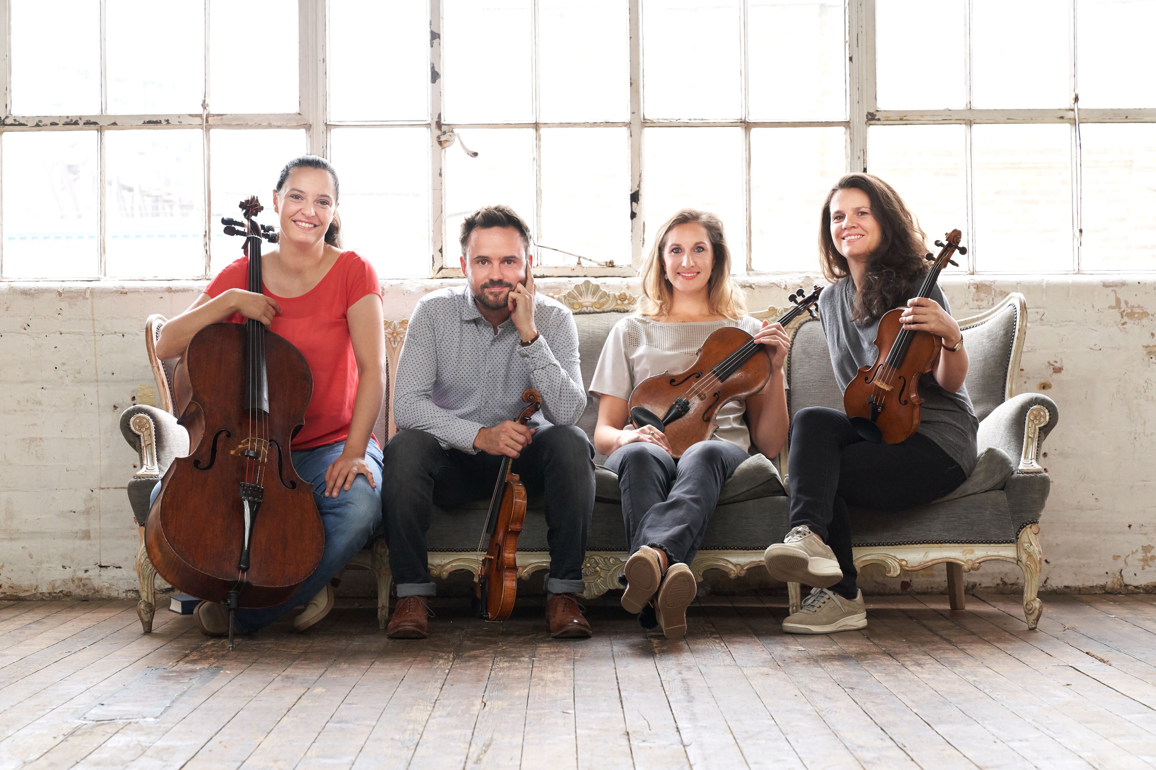 Elias String Quartet members sitting on a couch with violins, viola, and a cello.