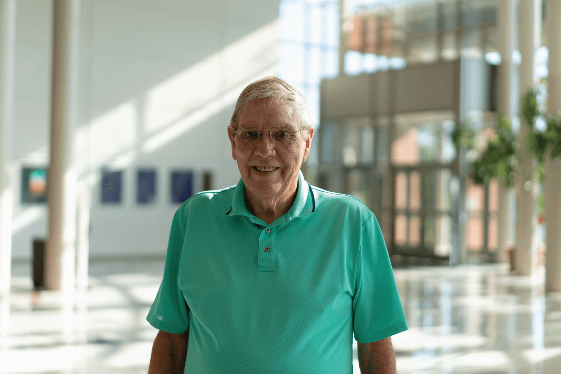 Carl wears a seaform green shirt and smiles standing in the empty lobby hall.