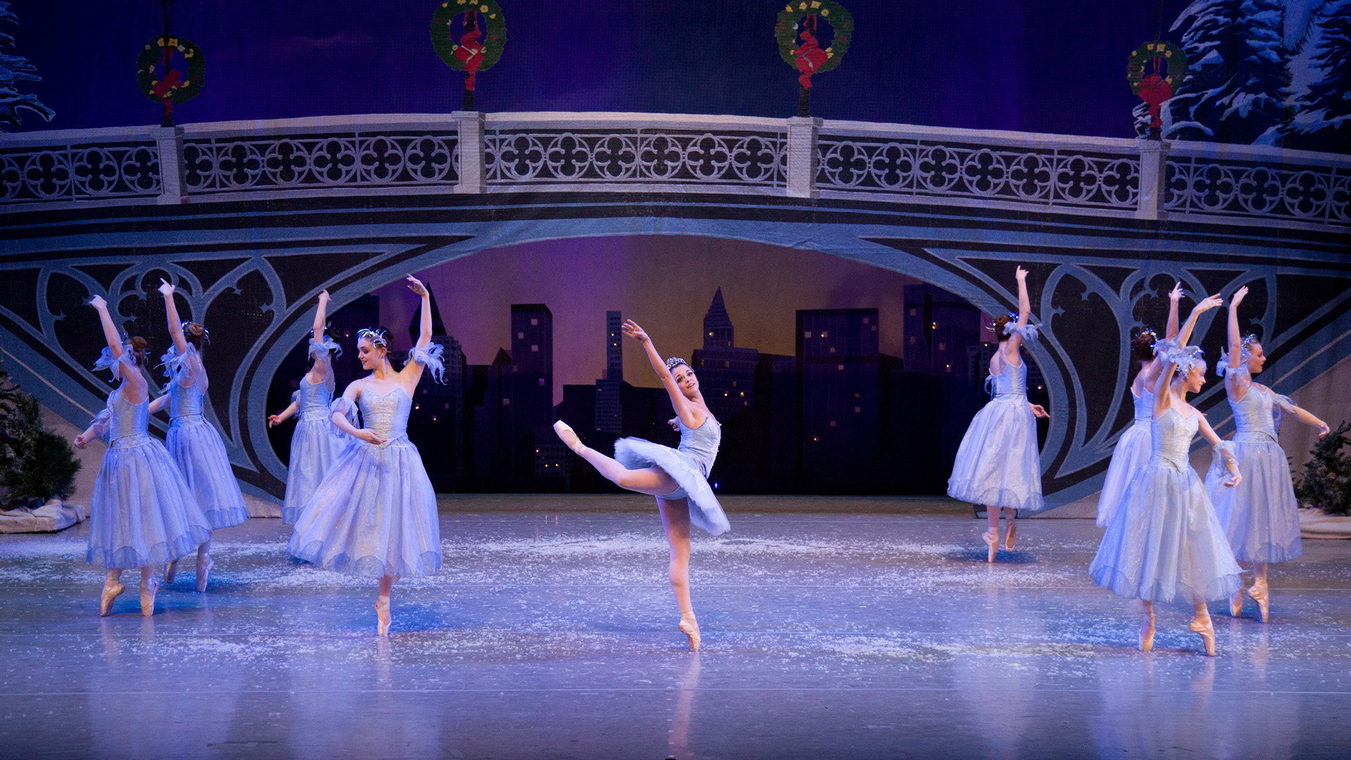 Young female ballet dancers dressed in pale blue tutus dance across a stage dusted with snow