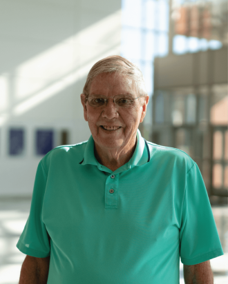 Carl wears a seaform green shirt and smiles standing in the empty lobby hall.