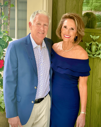 Terri and Steve in dress clothes standing and smiling in front of their home