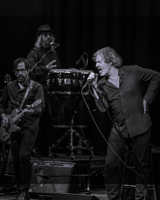 A man singing with a band in the background in black and white