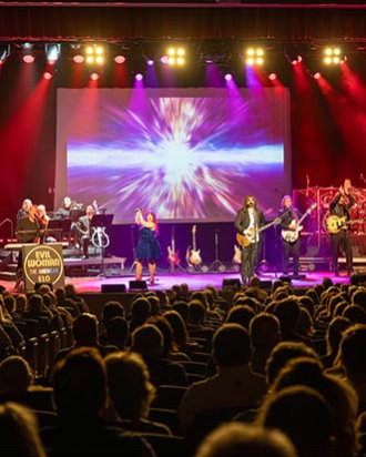 A group performing on stage with colorful lights. Text reads: Evil Woman The American ELO