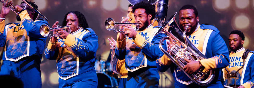 DRUMLine Live musicians perform with brass instruments in vibrant blue traditional marching band uniforms