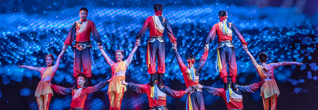 Circus performers pose in an acrobatic stack, linking arms together in an impressive physical feat